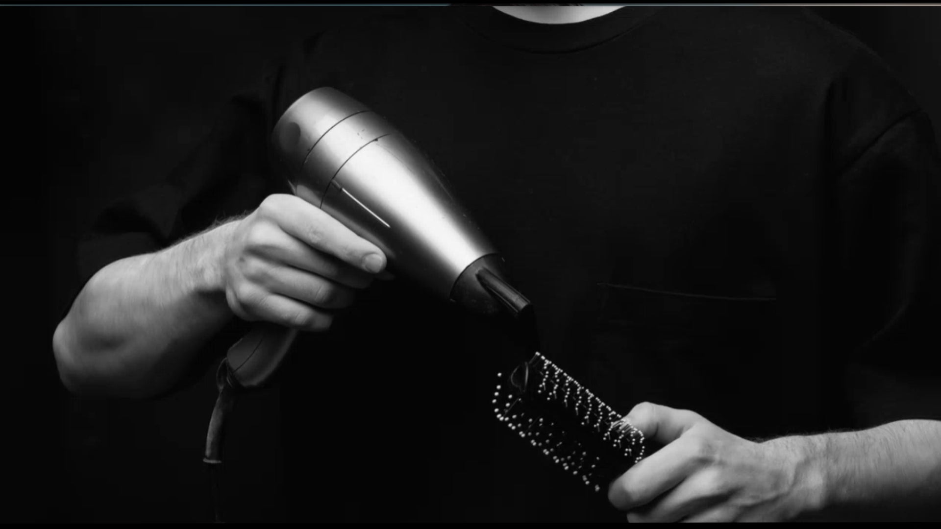 Person using a hair dryer and brush on a black background 